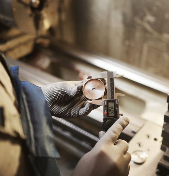 Tokarz mierzący obrabiany element za pomocą suwmiarki w warsztacie tokarskim, precyzyjna kontrola jakości.