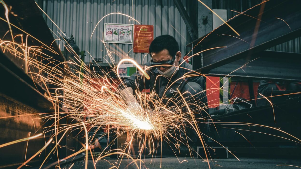 Tokarz lub frezer pracujący w warsztacie przemysłowym, wykonujący precyzyjną obróbkę metalu, otoczony jasnymi iskrami.