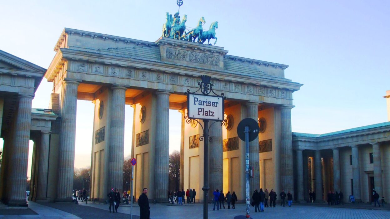 Brama Brandenburska w Berlinie oświetlona promieniami zachodzącego słońca, z widoczną tabliczką „Pariser Platz”