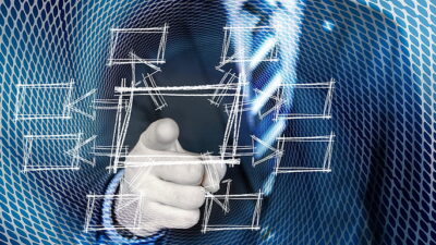 Osoba wskazująca palcem na wirtualny diagram procesów produkcyjnych z siatką technologiczną w tle