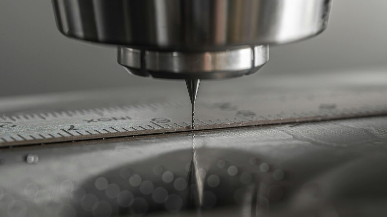 Zbliżenie na narzędzie skrawające maszyny CNC w trakcie obróbki metalu, z widoczną linijką pomiarową dla precyzyjnego cięcia.