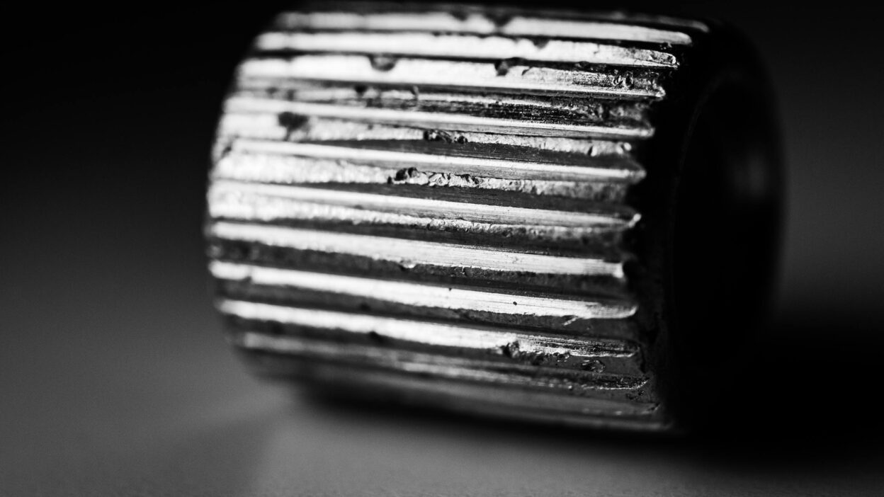Metalowy element z widocznymi rowkami, sfotografowany w czerni i bieli.