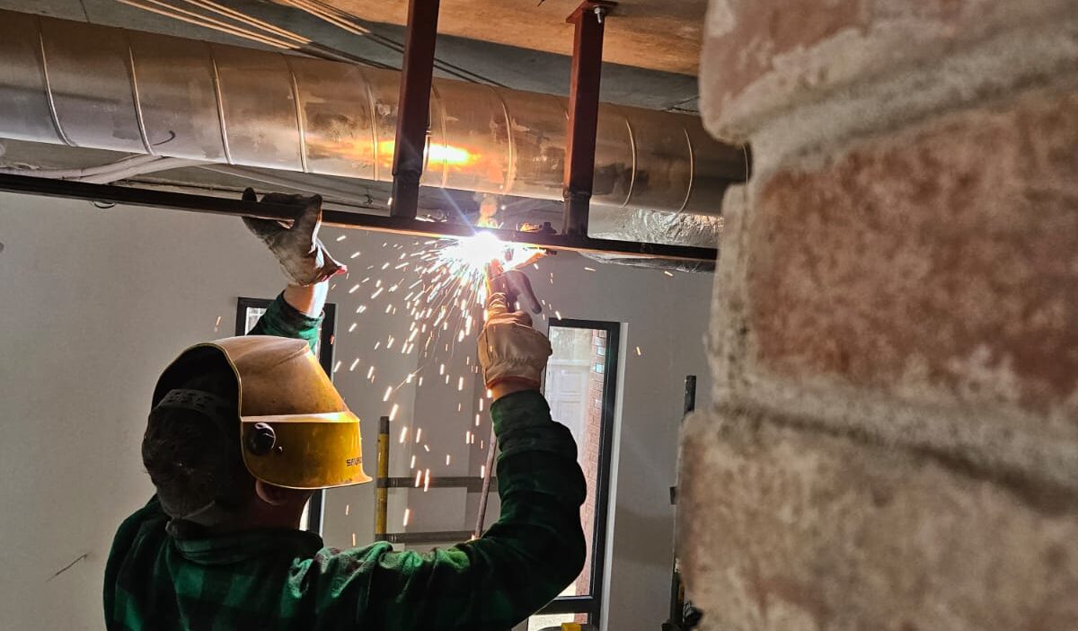 Spawacz TIG precyzyjnie łączy rurę ze stali nierdzewnej, obok spawacz MIG/MAG intensywnie pracuje nad konstrukcją stalową, z iskrzącym się łukiem.