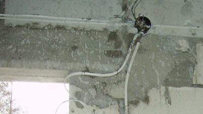 Instalacja elektryczna w ścianie z widoczną puszką i przewodami, symbolizująca wymagane uprawnienia SEP do pracy z elektryką.