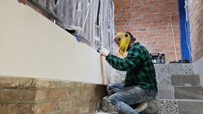 Spawacz w masce ochronnej i odzieży roboczej, spawający metalową konstrukcję przy schodach, ilustrujący praktyczny aspekt zawodu.